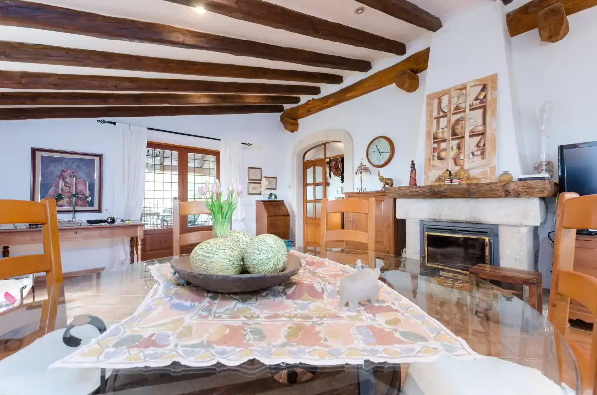 A living room with a fireplace, wooden ceiling beams, and a dining table.