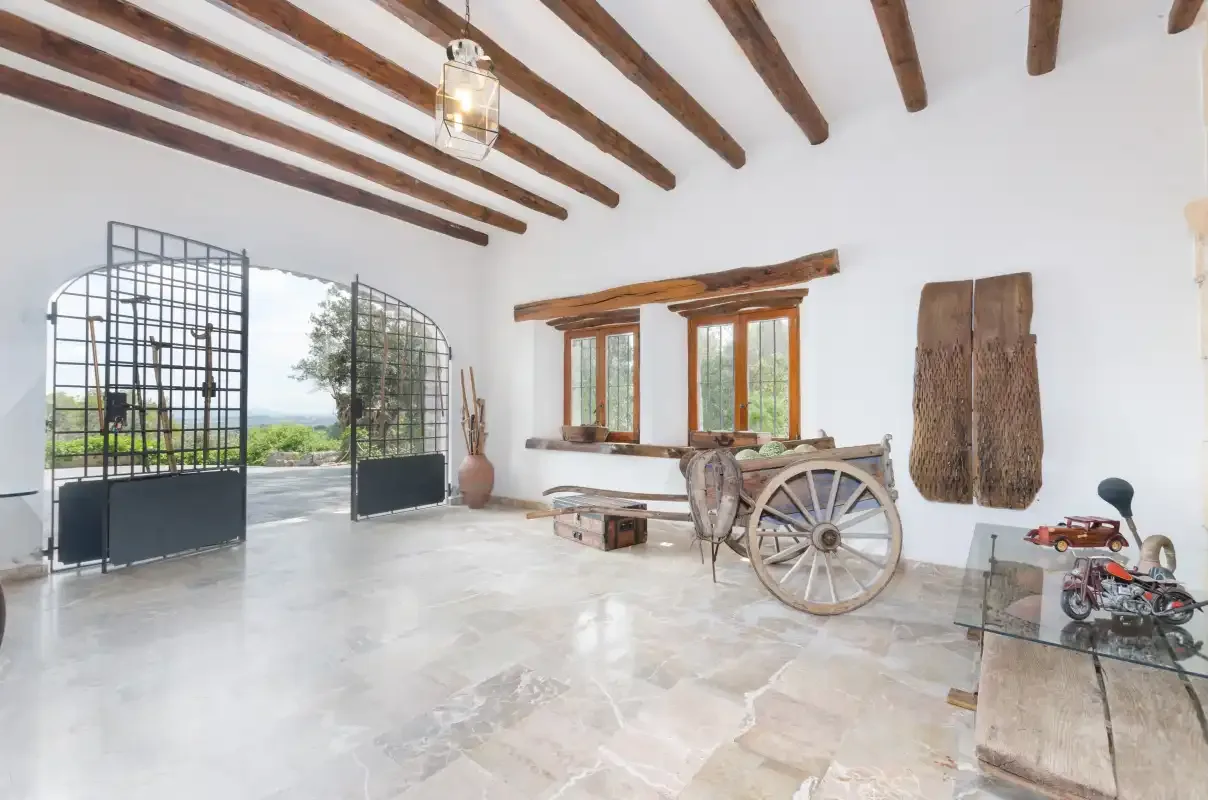 A bright interior room has exposed wooden ceiling beams and an open metal gate.