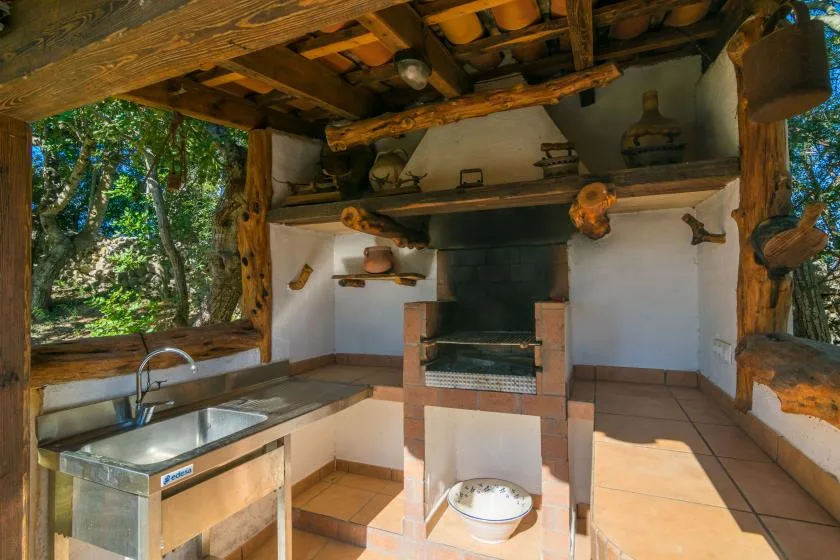 A rustic outdoor kitchen with a sink and a brick cooking hearth.