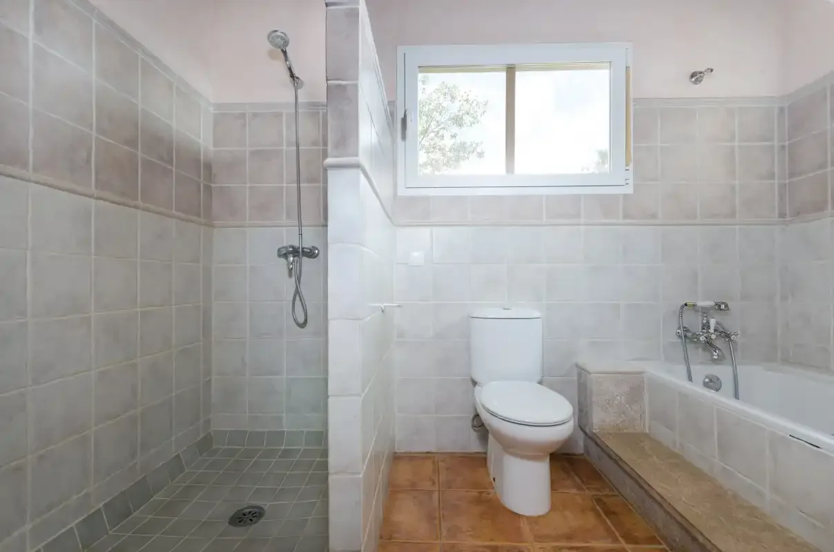 A tiled bathroom with a shower, toilet, and bathtub beneath a window.