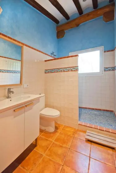 A tiled bathroom with a sink, toilet, and raised shower area.
