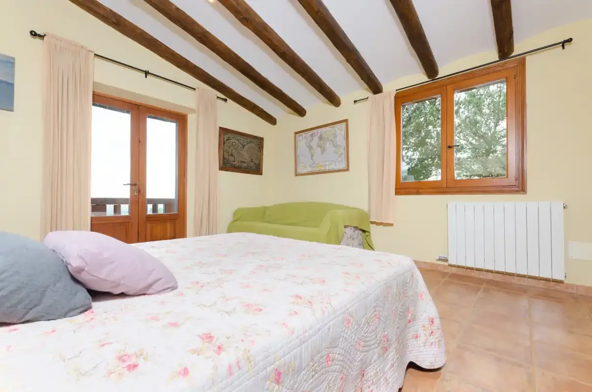 A bedroom with a large bed, wooden windows, and exposed ceiling beams.