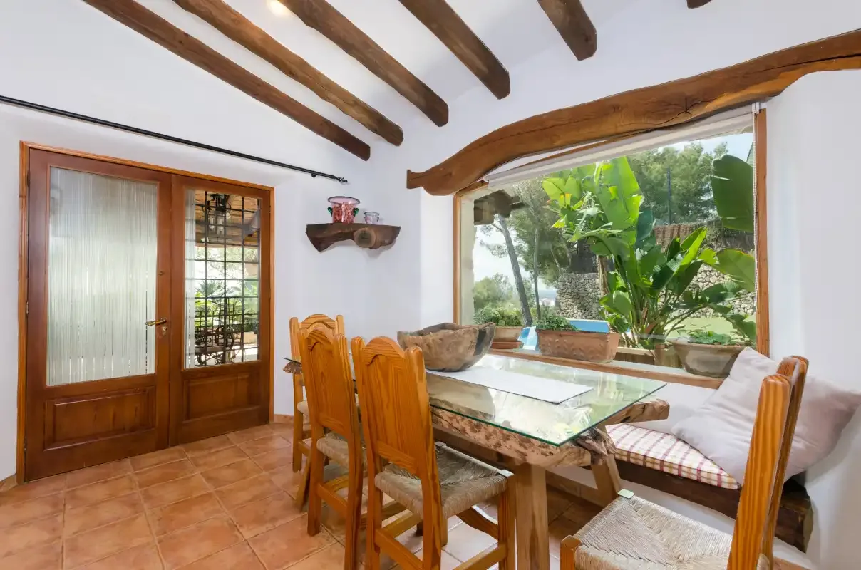 A dining area with a glass-top table and a large window overlooking greenery.