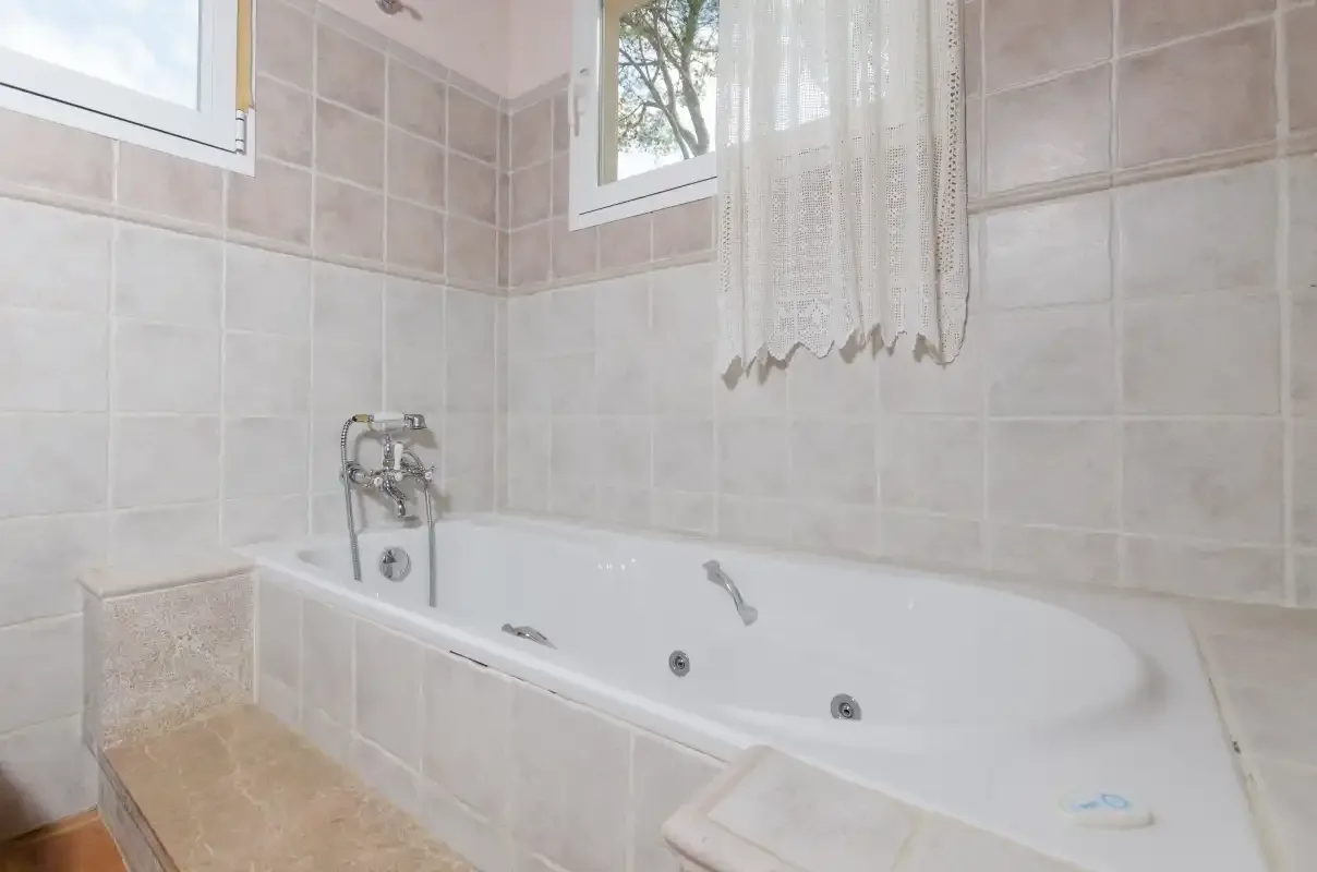 A tiled bathroom with a bathtub beneath two windows.