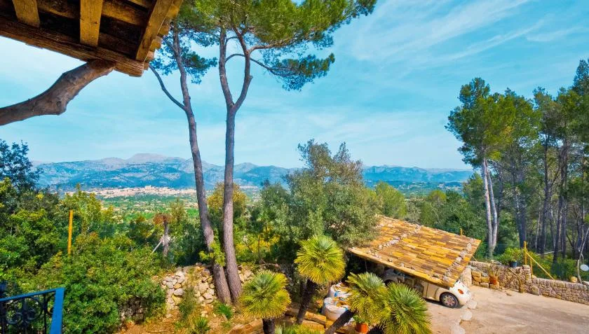A wooded hillside overlooks a distant valley, with a tiled-roof shelter in the foreground.