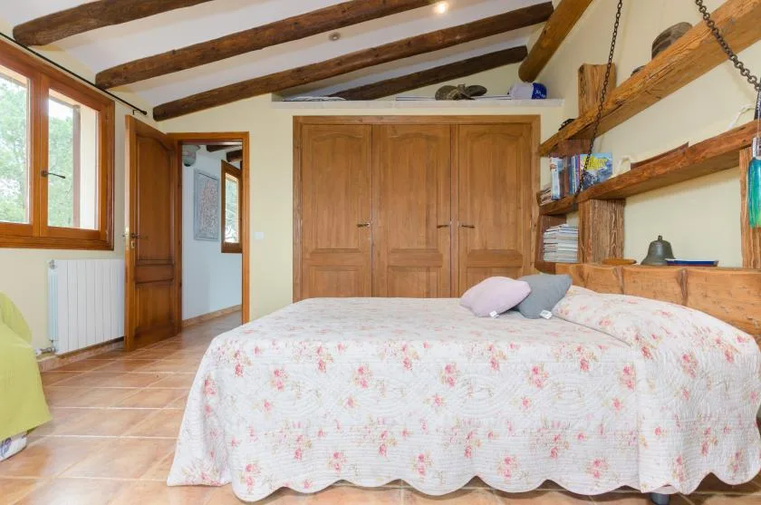 A bedroom with a floral bedspread and exposed wooden ceiling beams.