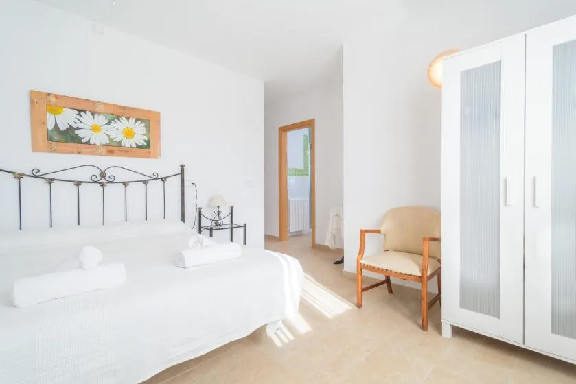A bright bedroom with a neatly made bed and a wooden armchair.