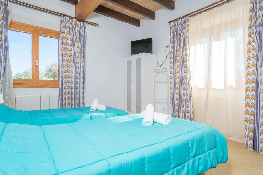 A bedroom with turquoise bedding, patterned curtains, and exposed wooden ceiling beams.