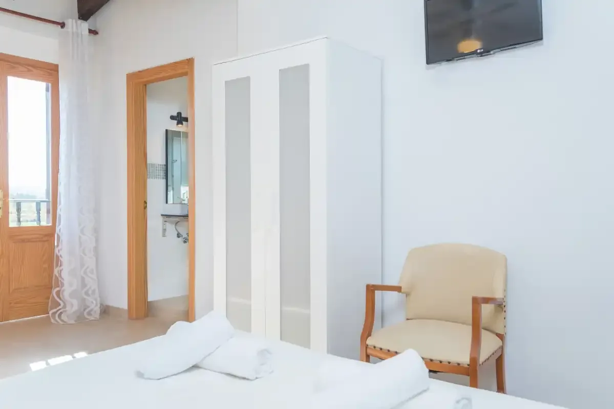 A bright bedroom with white bedding, a wardrobe, and a chair.