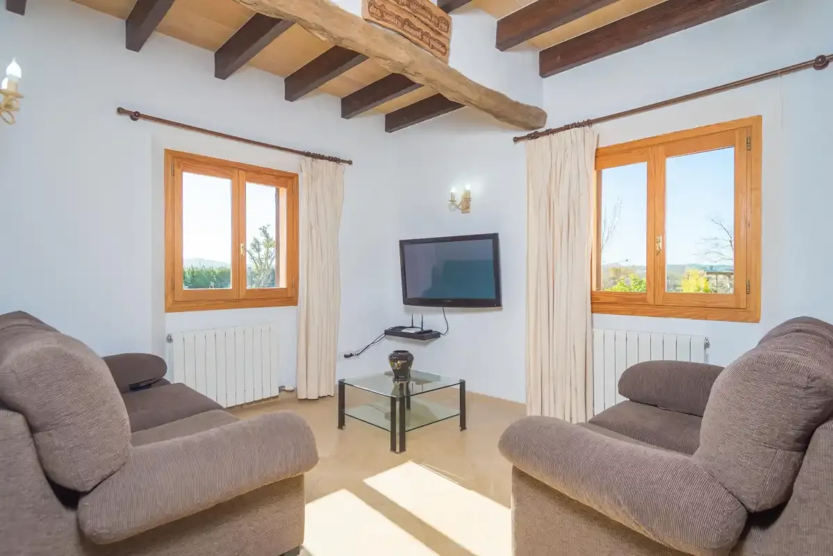 A living room with upholstered seating, a television, and exposed ceiling beams.