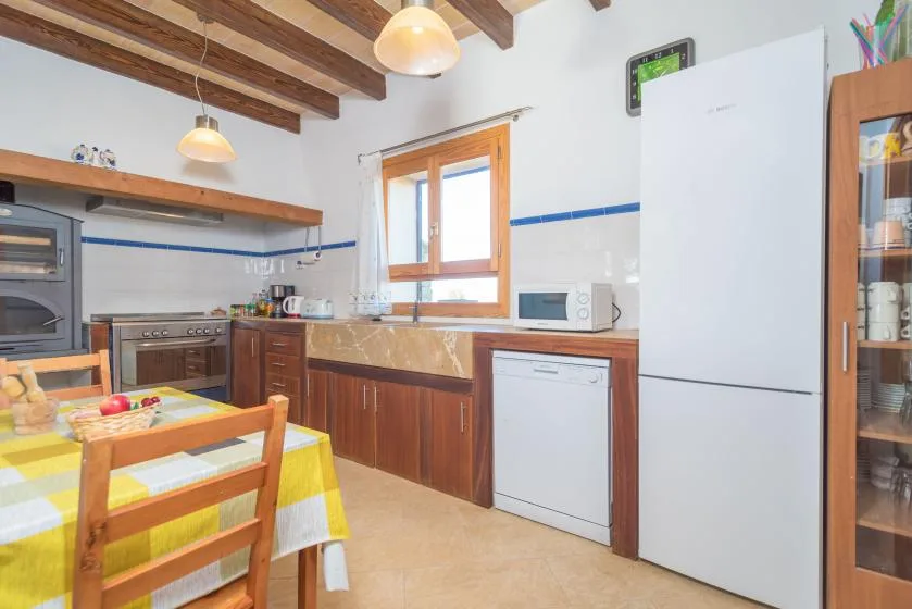 A kitchen with wooden cabinets, a dining table, and exposed ceiling beams.