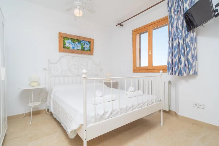A bright bedroom with a white bed beside a wooden-framed window.