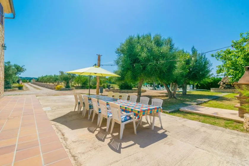 An outdoor dining area with a long table set beneath a yellow umbrella.