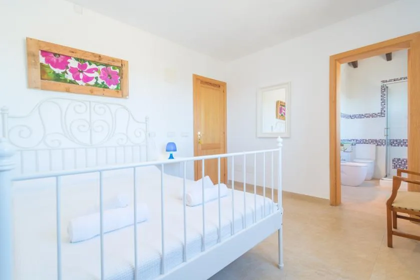 A bright bedroom with a white bed and a doorway opening onto a tiled bathroom.