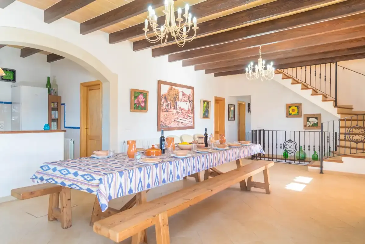 A dining area with a long table and benches beneath exposed ceiling beams.