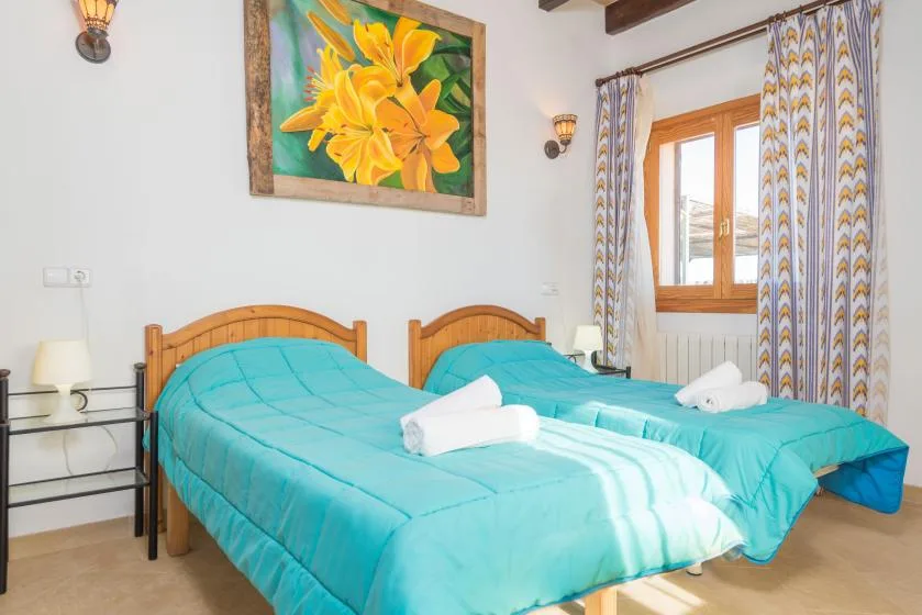 A bedroom with two beds covered in turquoise bedding and a window with patterned curtains.