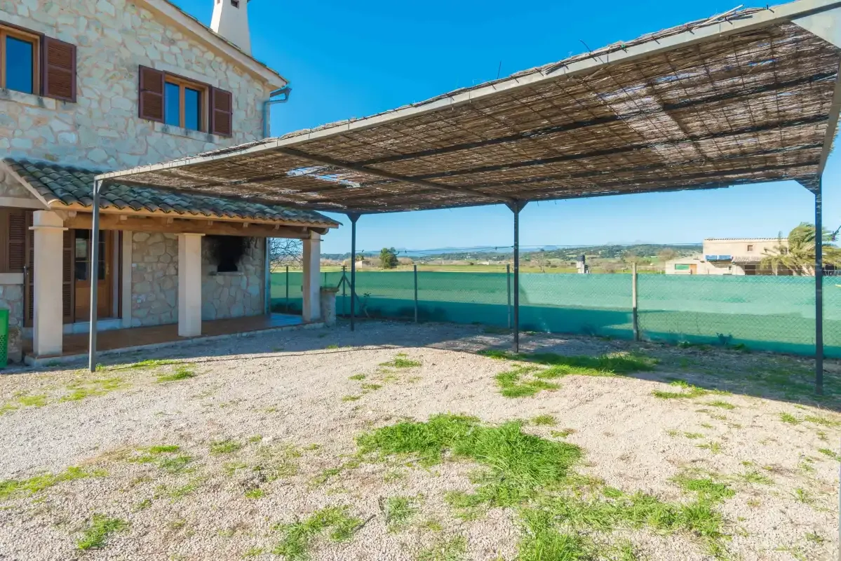 A covered outdoor patio beside a stone building overlooks open countryside.
