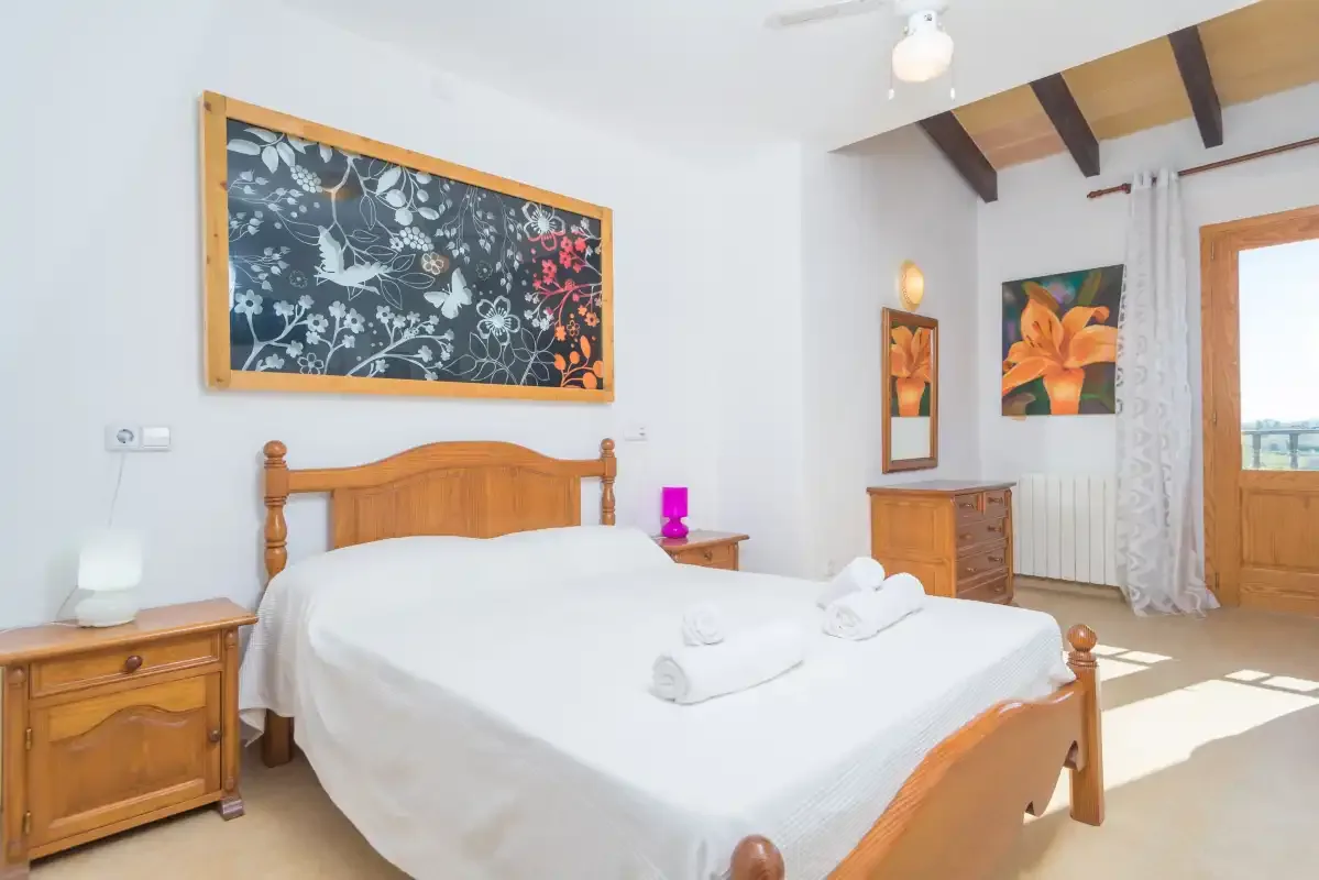 A bright bedroom with a wooden bed, white bedding, and floral wall art.