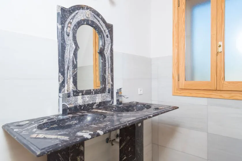 A bathroom vanity with a dark stone counter and a wooden-framed window.