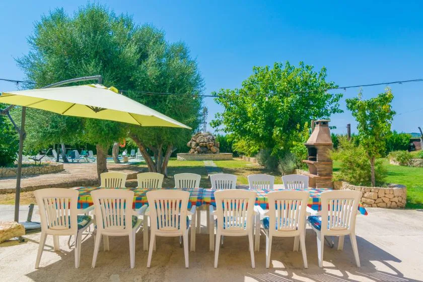 An outdoor dining area with white seating beneath a large sun umbrella.