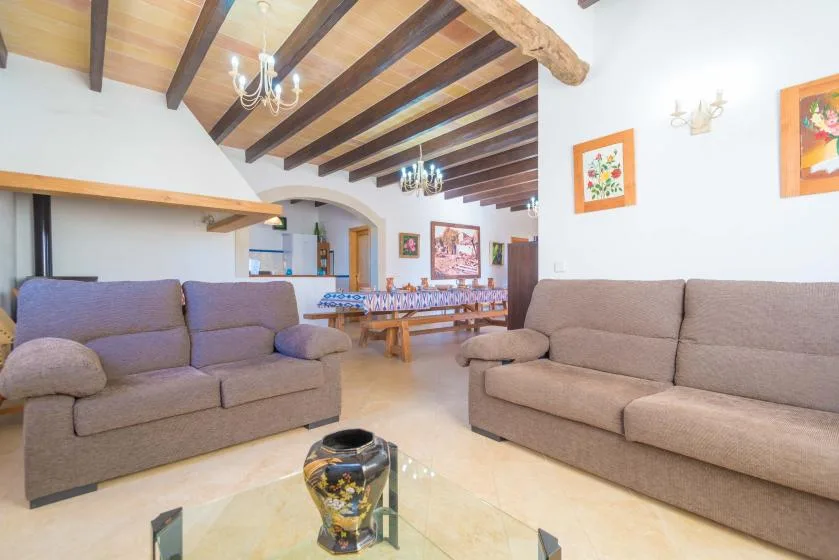 A living room with two seating areas and a dining table beneath exposed ceiling beams.