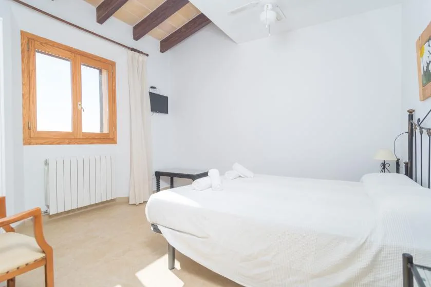 A bright bedroom with a large bed beneath exposed wooden ceiling beams.