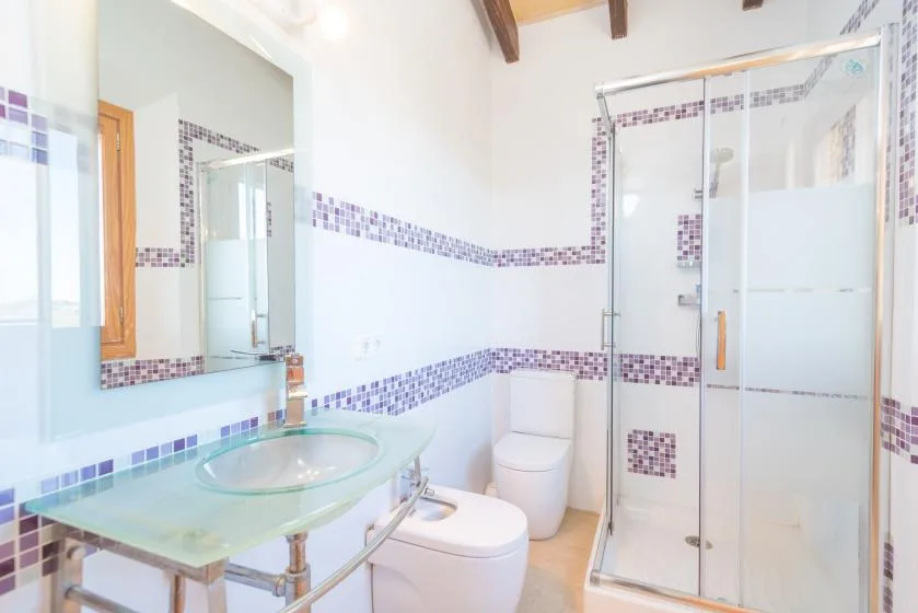 A bathroom with a glass shower, toilet, and sink.