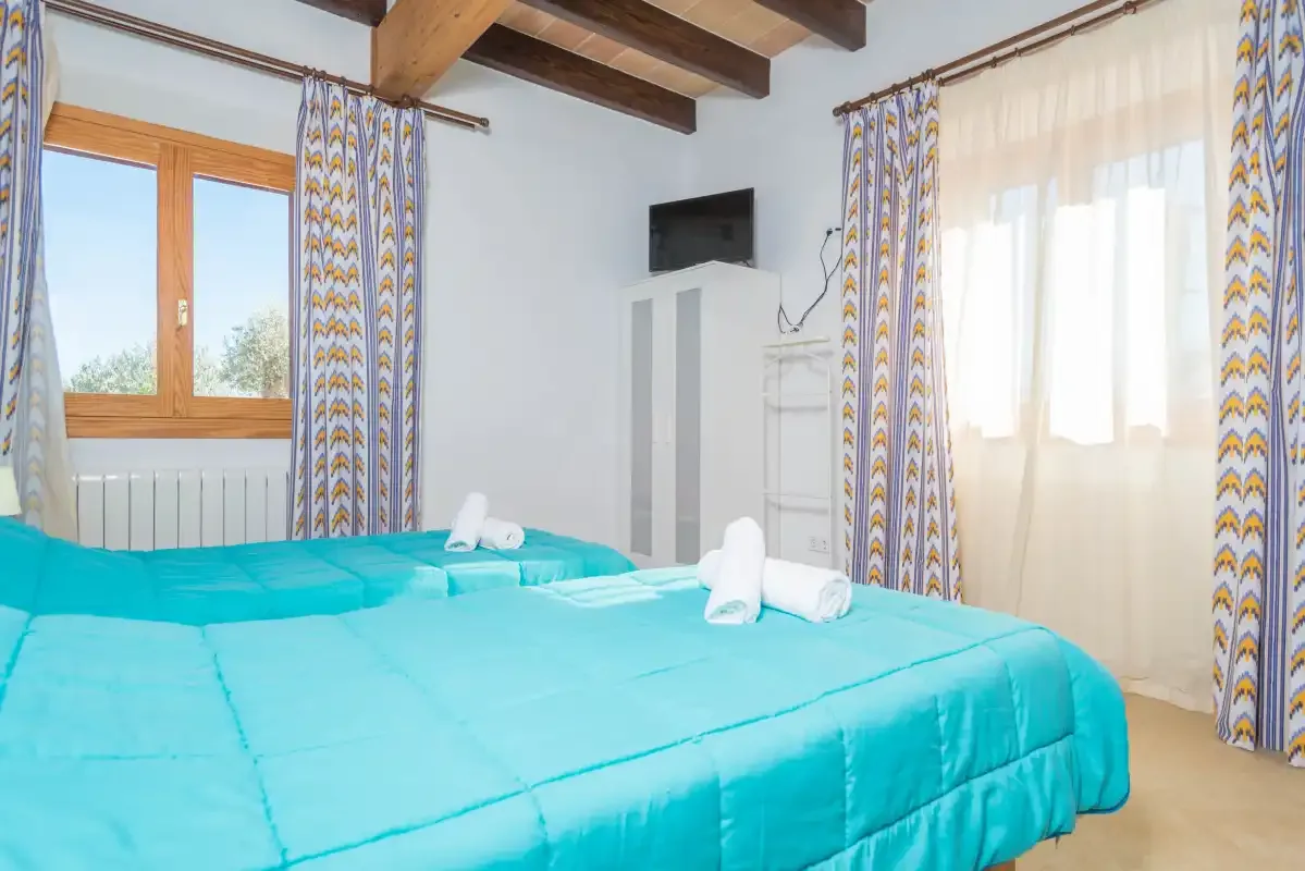 A bedroom with turquoise bedding, patterned curtains, and exposed ceiling beams.