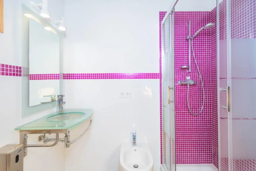 A bright bathroom with a glass shower and pink tile accents.