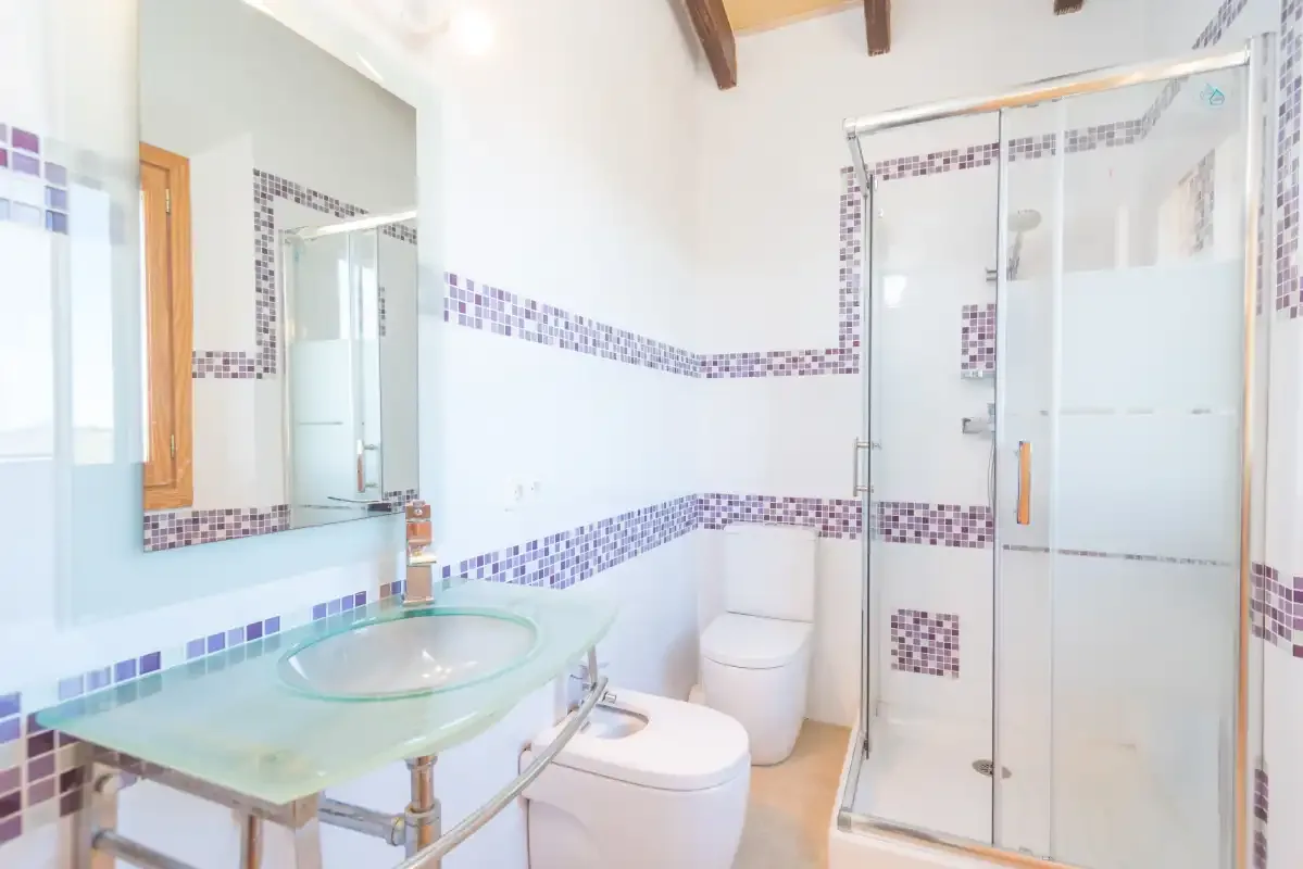 A bright bathroom with a glass sink and a shower.