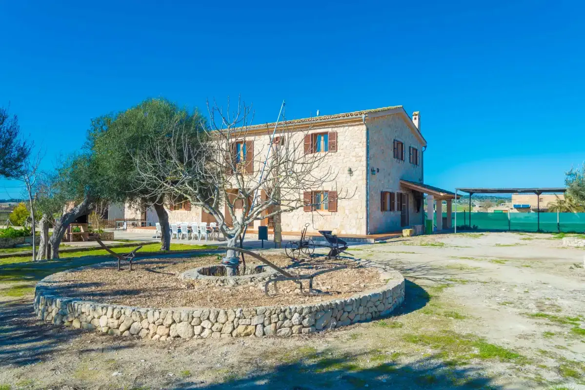 A two-story house stands beside a stone-edged garden under a clear blue sky.