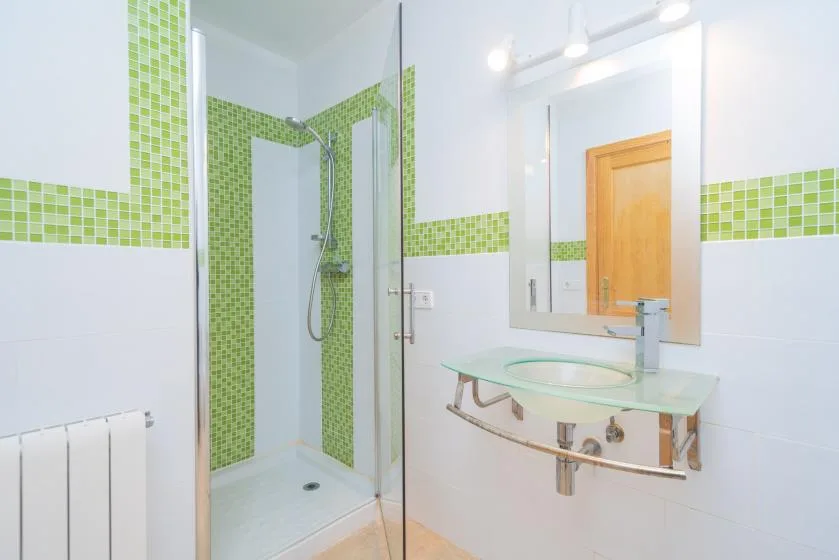 A bathroom with a glass shower, green tile accents, and a sink beneath a mirror.