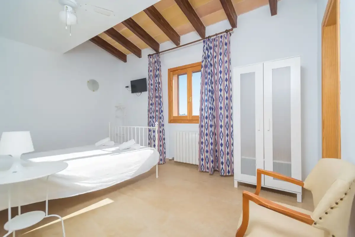 A bright bedroom with two beds, patterned curtains, and exposed ceiling beams.