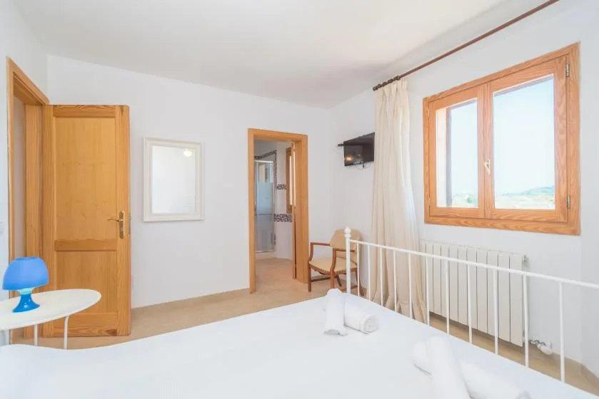 A bright bedroom with a white bed beside a large window.