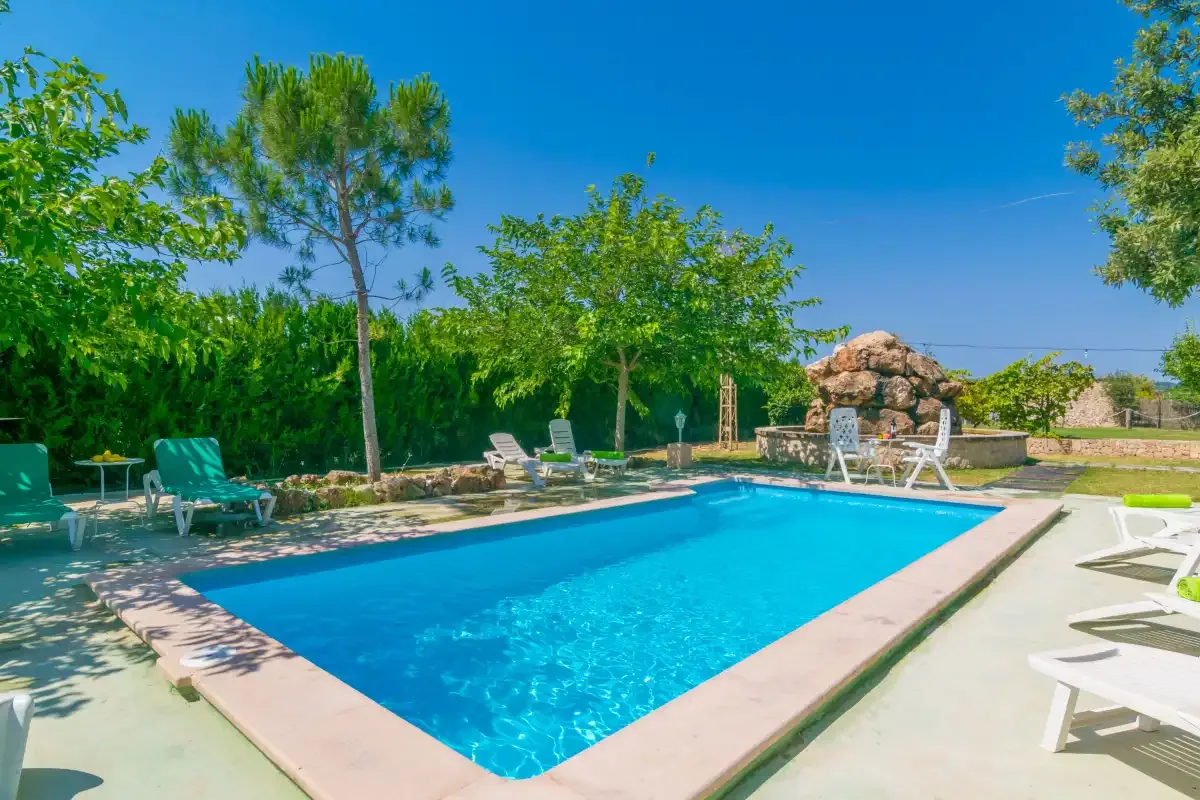 An outdoor swimming pool surrounded by trees and lounge seating.