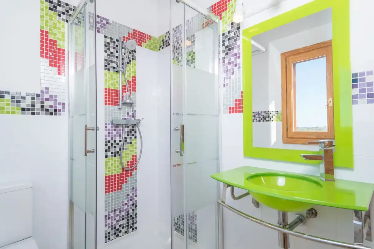 A bright bathroom with a glass shower and a green sink counter.