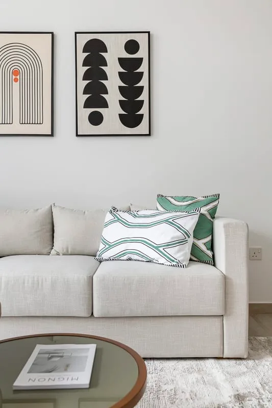 Una sala de estar con un sofá claro y láminas abstractas enmarcadas.