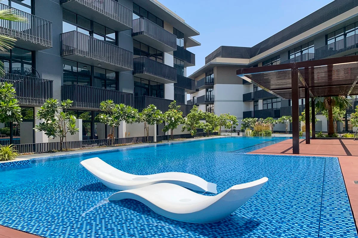 Una piscina entre edificios modernos, con tumbonas blancas escultóricas dentro del agua.