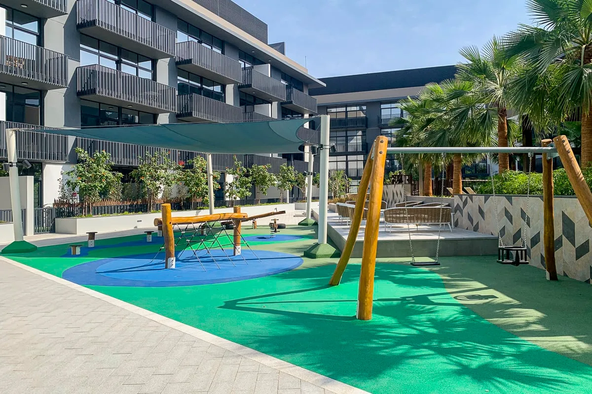 Un parque infantil al aire libre tiene un suelo de goma colorido y una estructura de columpio de madera.