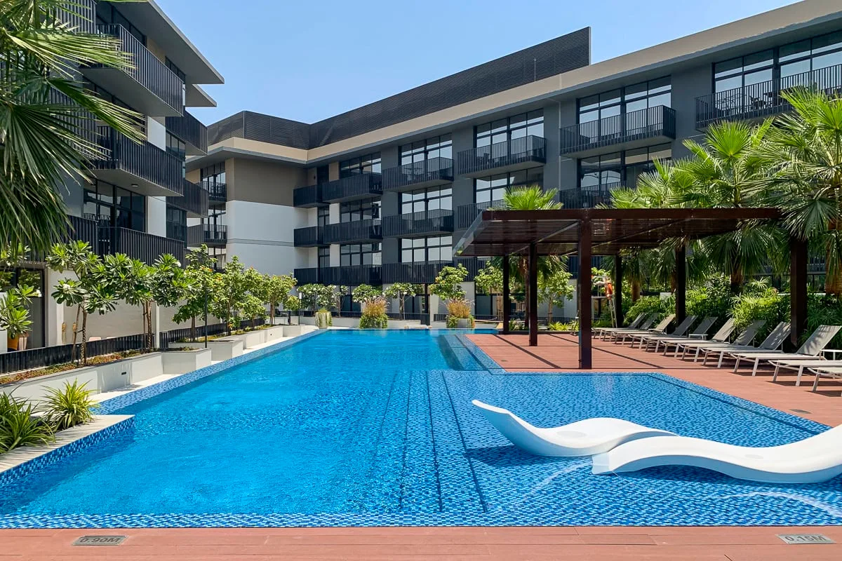 Una piscina rodeada de edificios modernos, tumbonas y plantas tropicales.