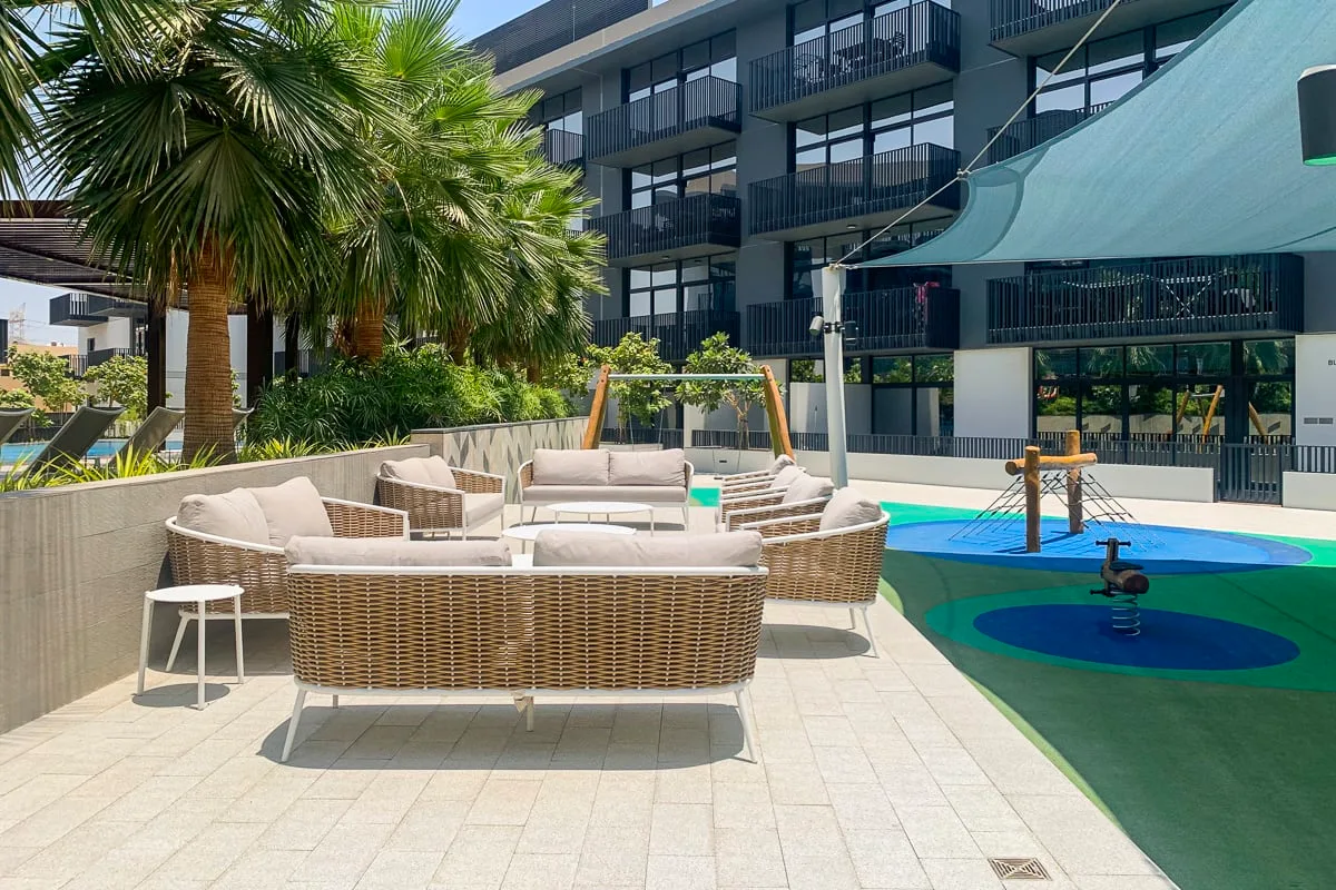 Un patio al aire libre con asientos tejidos junto a una piscina colorida y un edificio moderno.