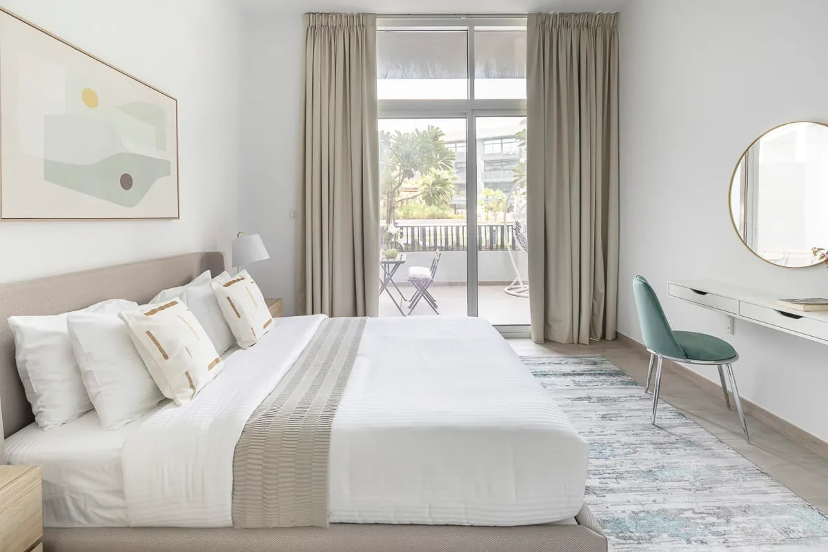 Un dormitorio luminoso con una cama bien tendida y puertas corredizas de vidrio que dan a un balcón.