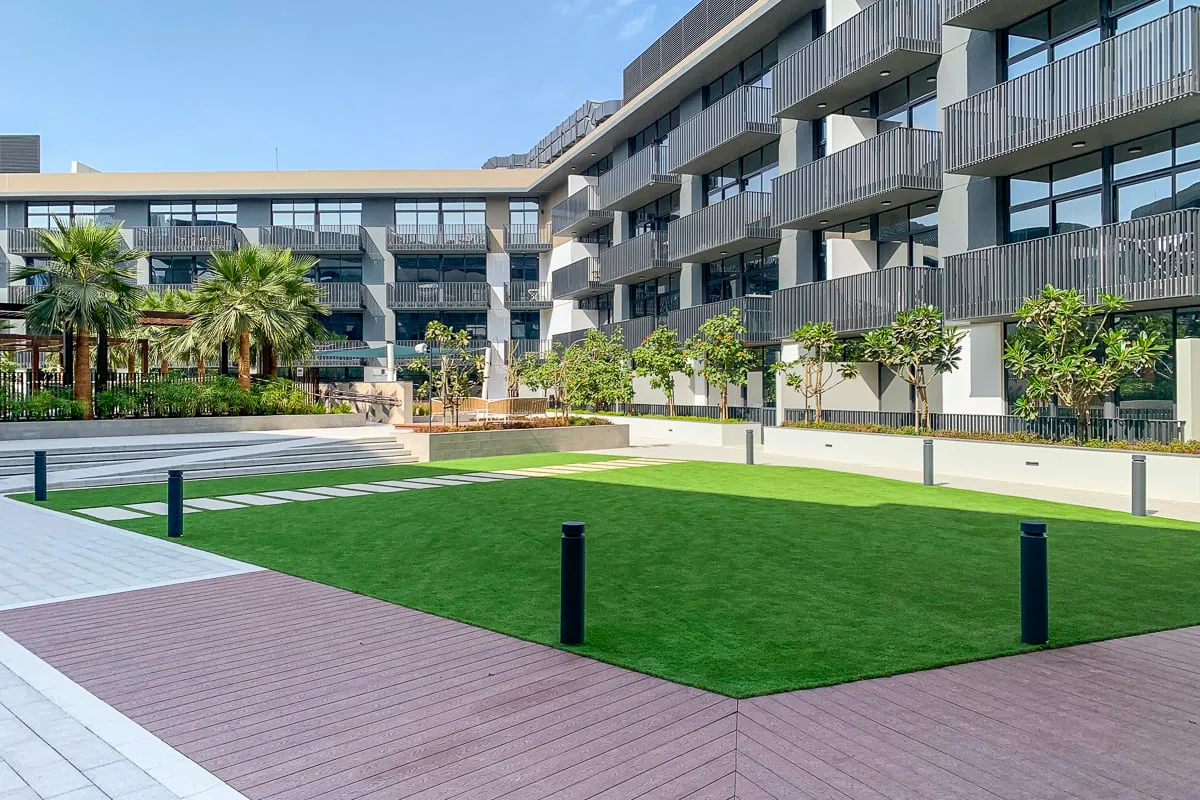 Un patio ajardinado con césped, caminos pavimentados y edificios de apartamentos modernos.