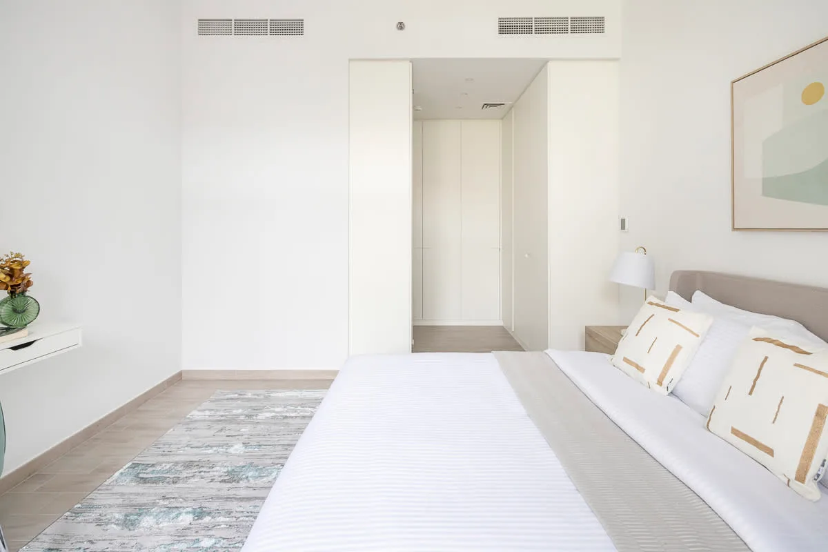 Un dormitorio luminoso con una cama tendida y una lámina abstracta enmarcada.