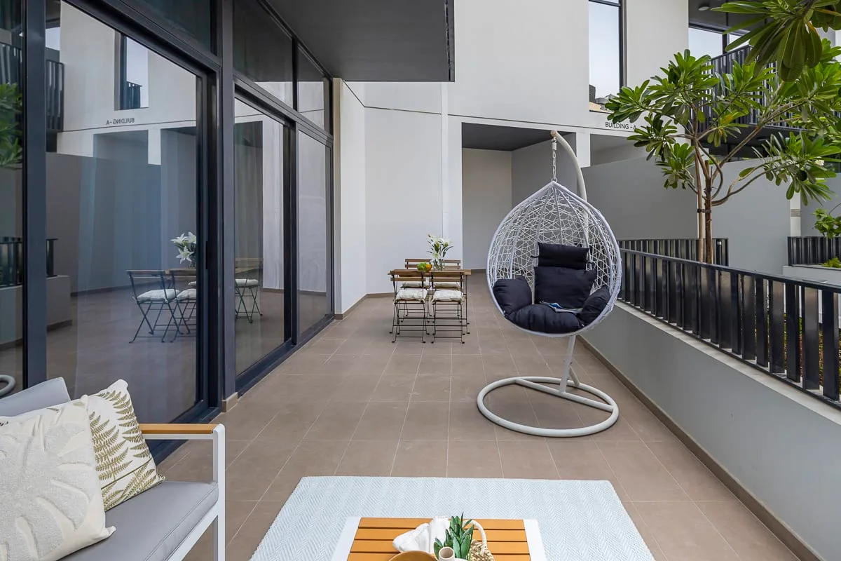 Una terraza moderna al aire libre con una silla colgante, asientos y plantas en macetas.
