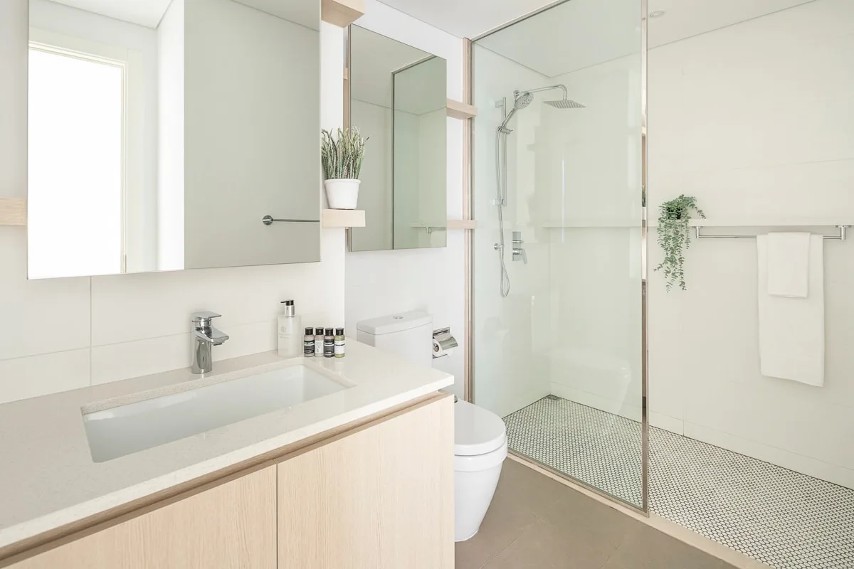 Un baño luminoso con un lavabo largo y una ducha de cristal.