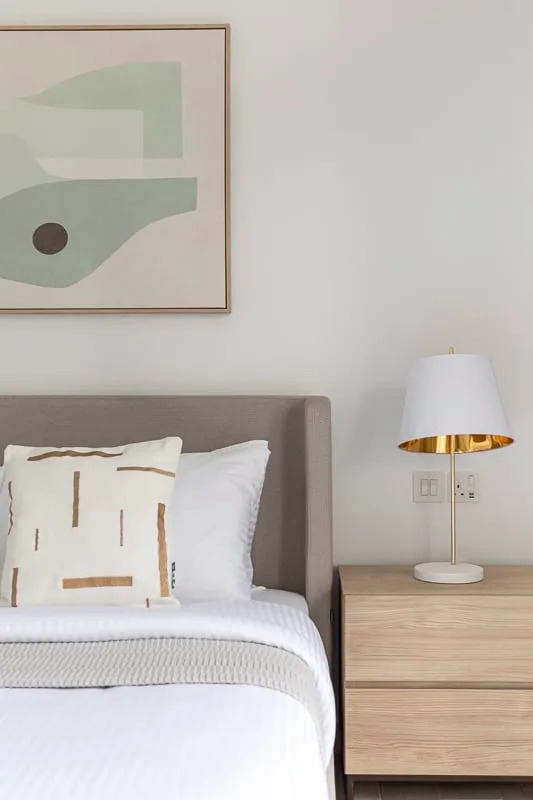 Un dormitorio con una cama tendida, arte abstracto enmarcado y una lámpara de noche.