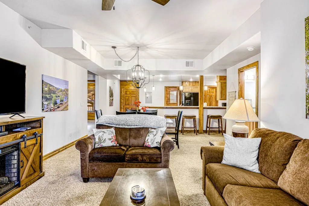 A living room with seating, a television, and a kitchen counter in the background.