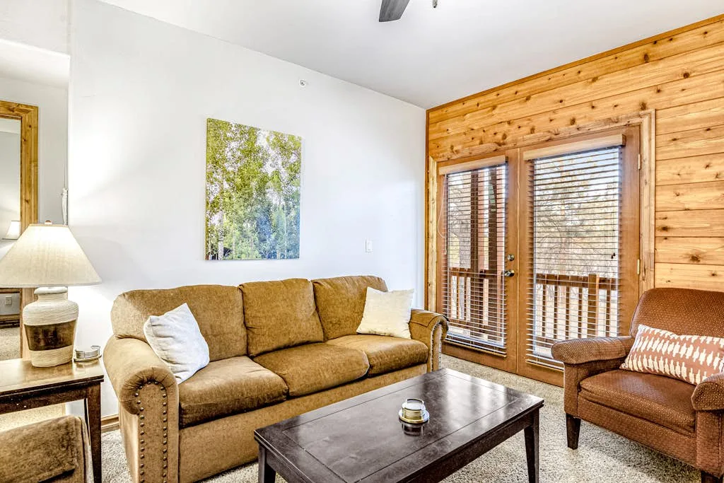 A living room with a tan sofa, a coffee table, and large windows.
