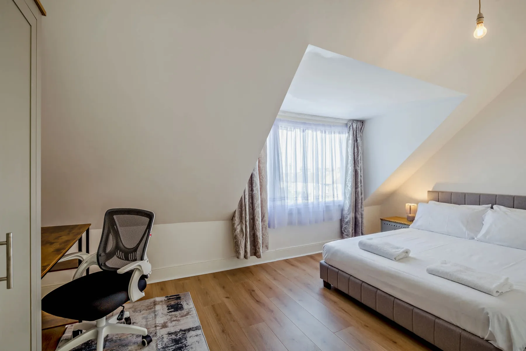Un dormitorio con una cama, un escritorio y una ventana con cortinas.
